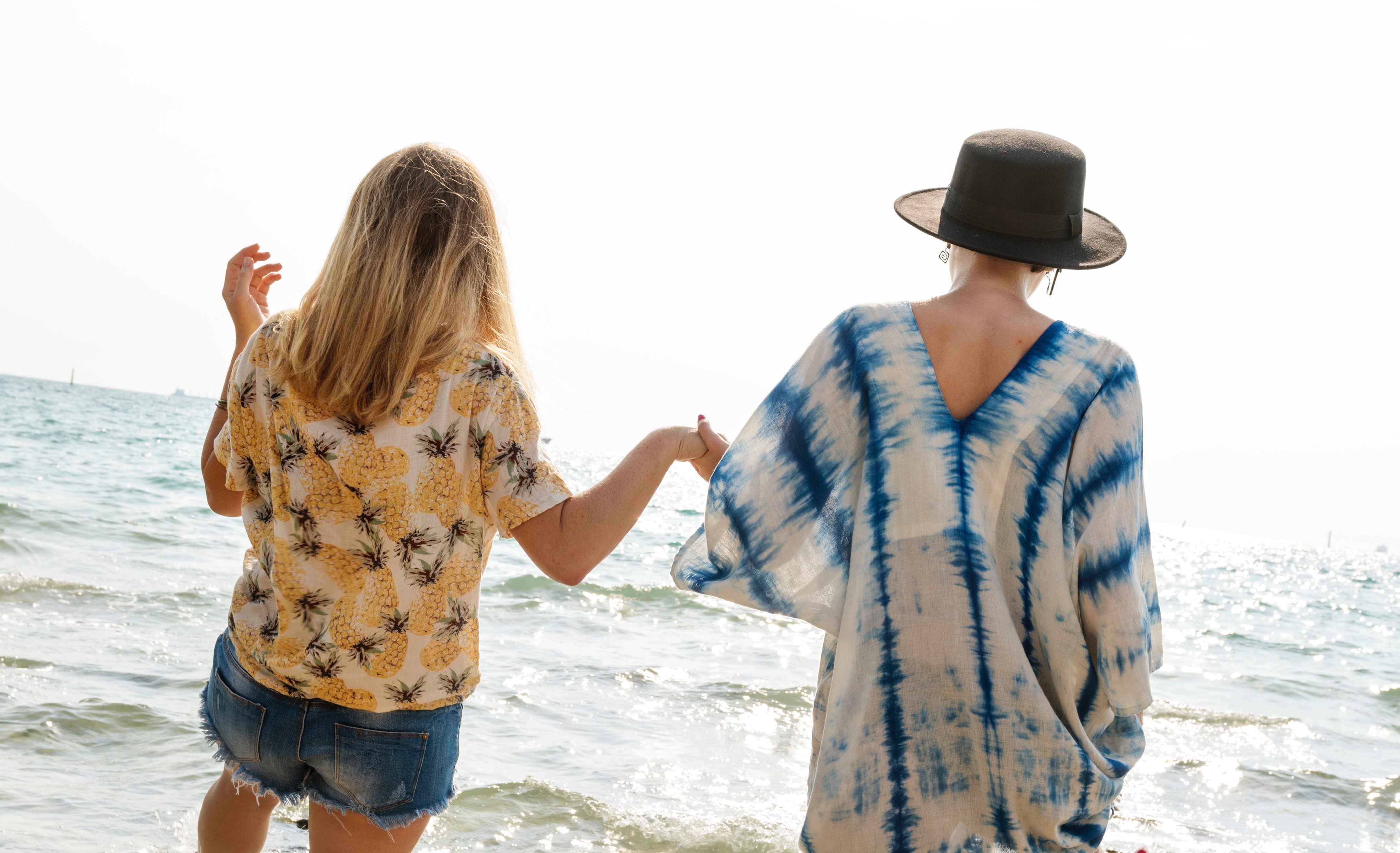 Två kvinnor håller handen på stranden